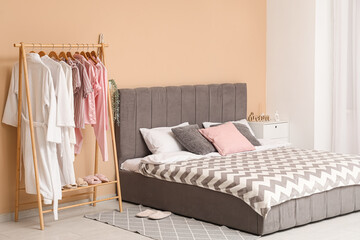 Comfortable bed and rack with clothes in interior of bedroom