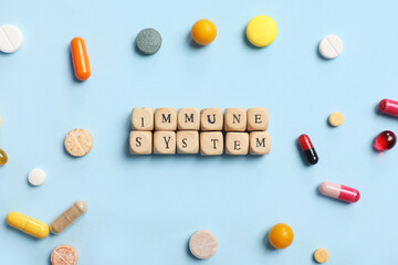 Composition with text IMMUNE SYSTEM made of wooden cubes and different pills on color background