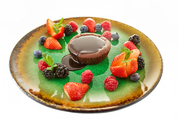 Cocoa soufflé with chocolate sauce, served with raspberries, strawberries, blackberries and blueberries on a decorative plate, white background