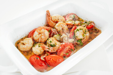 Baked shrimp with tomatoes, onions, parsley and garlic in a ceramic dish, on a white background