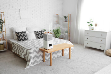 Interior of bedroom with shelving unit and modern humidifier on wooden bench near bed