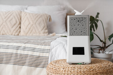 Modern humidifier on wicker ottoman near bed in bedroom