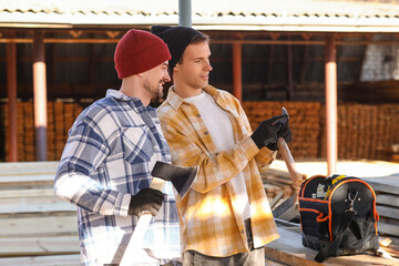 Male carpenters with axes at sawmill