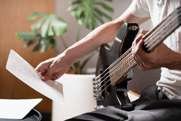 Man sitting studying sheet music for electric bass with a musical instrument on his lap.