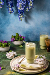 Iced matcha latte decorated with flowers and sage on green table