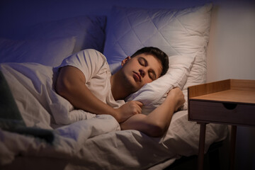 Handsome young man sleeping on bed in evening at home