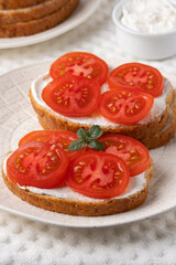 Delicious open-faced sandwiches topped with fresh tomatoes and cream cheese served on a textured white plate