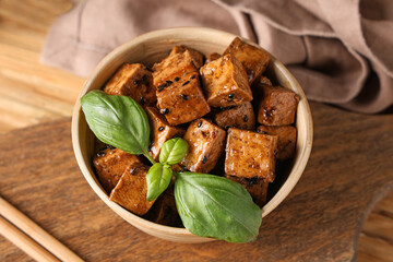 Bowl with pieces of fried tofu cheese and basil on wooden background, closeup