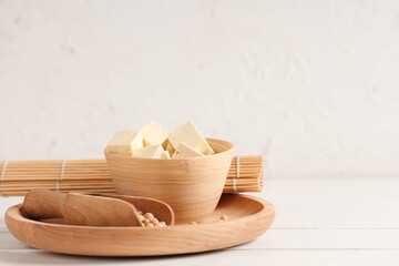 Bowl with pieces of tofu cheese on white wooden background