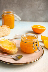 Plate with slices of bread and jar of sweet orange jam on light blue table