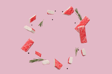 Frame made of cut tasty crab sticks with peppercorns and rosemary flying on pink background © Pixel-Shot