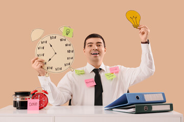 Young businessman with paper alarm clock and light bulb at table on beige background. Time management concept