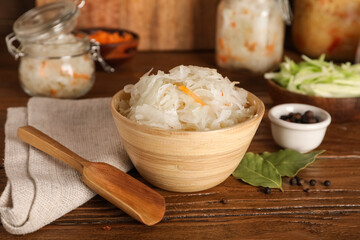 Tasty sauerkraut in bowl with condiments on wooden table. Closeup