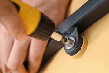 Male carpenter tightening screw in wooden table with screwdriver, closeup