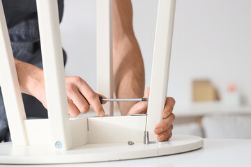 Male carpenter tightening screw in table with screwdriver, closeup