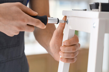 Male carpenter tightening screw in white wooden furniture with screwdriver, closeup