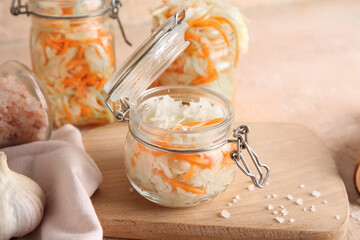 Glass jars with tasty sauerkraut and bottle of salt on table against beige background. Closeup