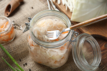 Glass jar with tasty sauerkraut and ingredients on wooden table. Closeup
