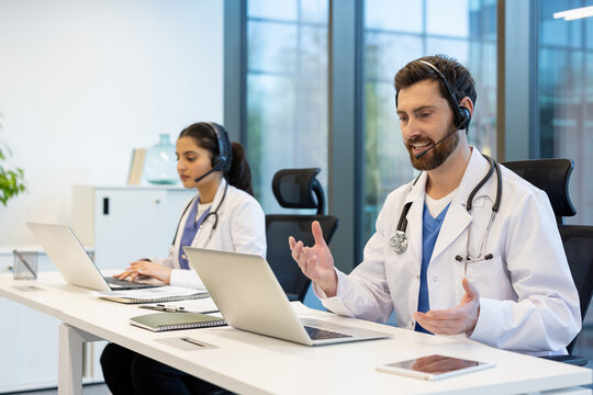 Two doctors working remotely consulting patients remotely, man and woman with headset using laptop for video call, working inside clinic, patient support and assistance service.