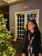 Very pretty older woman with a tiara on her head that says happy new year looking at a lit up...