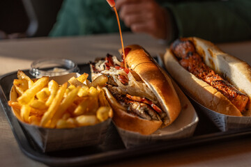 Hand adding ketchup to hot Spanish sandwich.