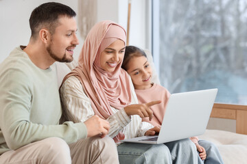 Muslim parents with their daughter using laptop at home