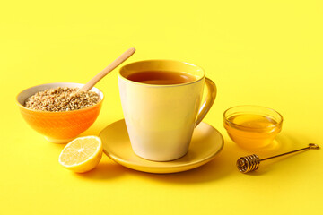Cup of hot buckwheat tea with lemon and bowl of honey on yellow background