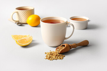 Cups of hot buckwheat tea with lemon and bowl of honey on grey background