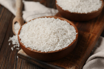 Bowls and scoop with raw rice on wooden background, closeup
