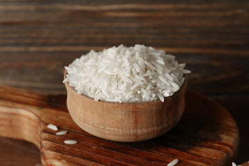 Bowl with raw rice on wooden background, closeup