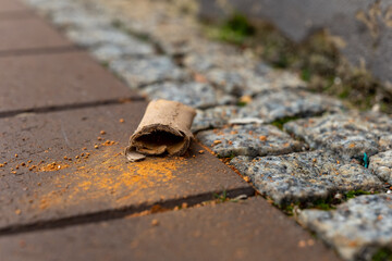 Discarded paper roll on urban sidewalk near stone pavement showing traces of orange powder