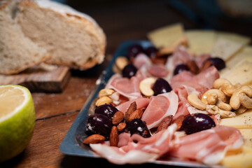 Charcuterie board close-up with bread loaf in the background, olives, almonds, prosciutto