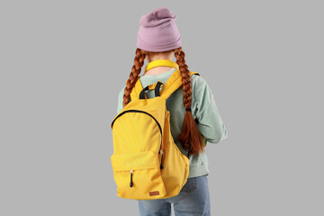 Teenage redhead girl with backpack on light background, back view