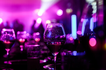The bride fastens heGlass with drops of wine on a background of neon lightr high-heeled shoes