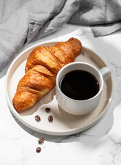 Cup of  espresso coffee and fresh croissant on white plate on marble background with shadow and napkin.