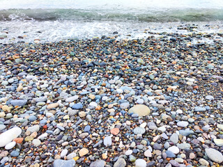Colorful pebbles on a shoreline at low tide with gentle waves lapping against the shore