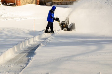 Side view of a man using a snow blower to begin clearing a residential driveway