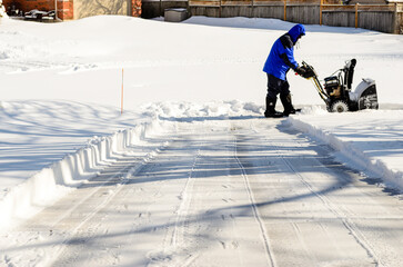 Man using a snow blower to finish clearing most of a residential driveway