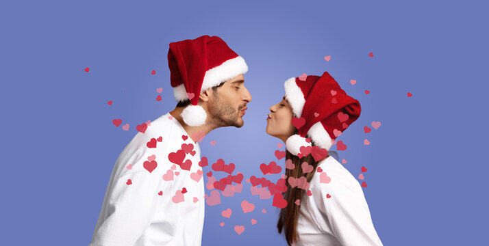 A couple in matching Santa hats leans in to share a loving kiss, surrounded by heart-shaped decorations. Their joyful expression captures the spirit of celebration during the holiday season.