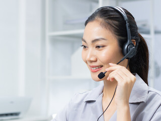 Friendly Asian woman working as a customer support operator with a headset in a call center office. Portrait of female sales agent talking to client working at desk. Customer service representative.