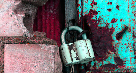 Rusty padlock hangs on a weathered door in a neglected urban area during daylight hours