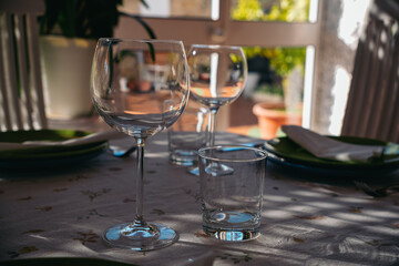 Elegant empty wine and water glasses resting on a table set with plates, cutlery, and napkins, illuminated by natural light