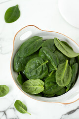 Fresh baby spinach leaves in a dish isolated on white marble background. Top view.