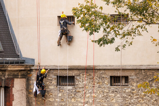 Deux travailleurs cordistes r&eacute;novent une fa&ccedil;ade d'immeuble &agrave; Paris
