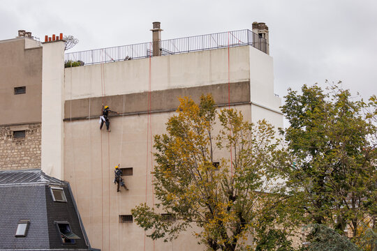 Deux travailleurs cordistes r&eacute;novent une fa&ccedil;ade d'immeuble &agrave; Paris