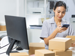 Asian female small business shop owner using application on smartphone scanning QR code on parcel...