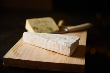 Wooden board with assorted delicious gourmet cheeses in evening light
