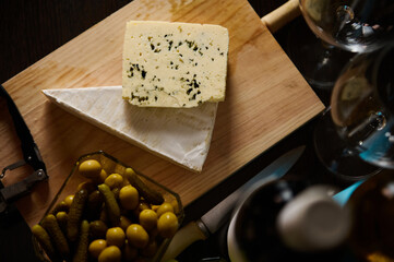 Elegant cheese board with cheese, pickles, and wine glasses on wooden background