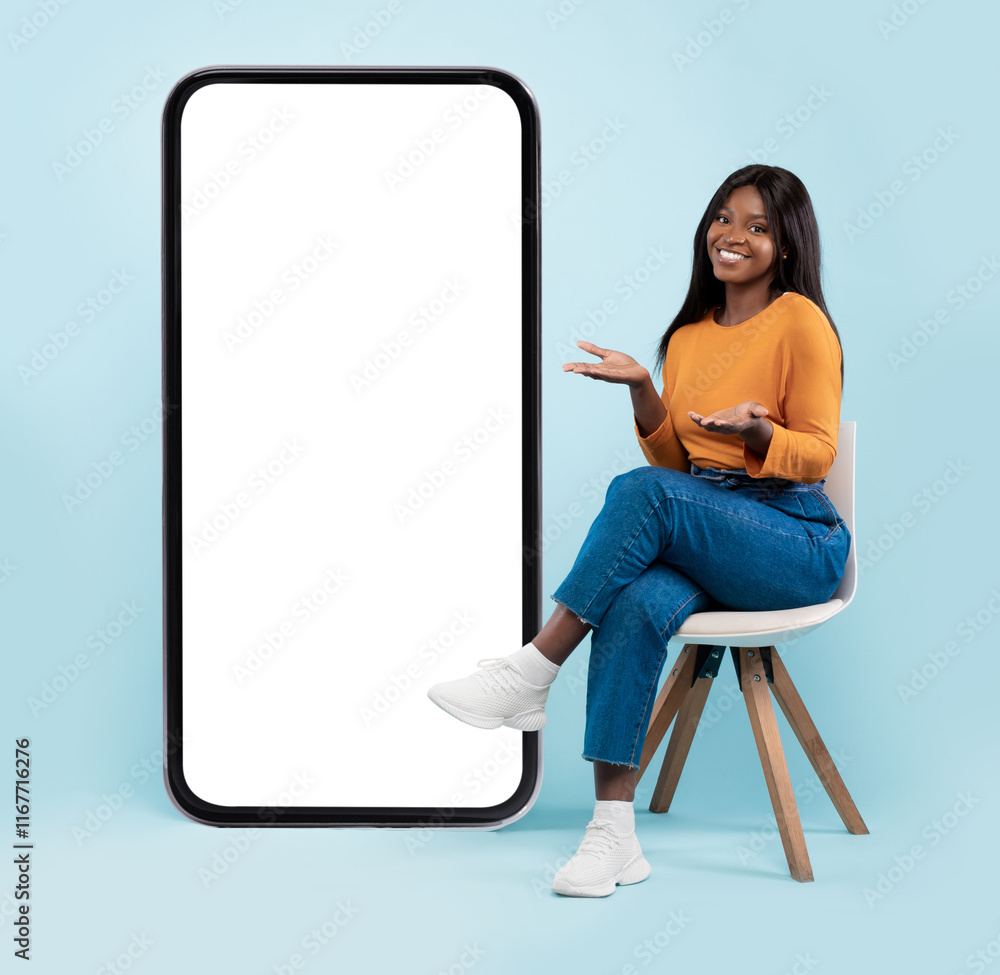 Poster full length of pretty black lady sitting on chair next to big blank smartphone with mockup for mobil