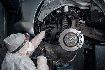 An auto mechanic applies anti-corrosion mastic to the underbody of a car.